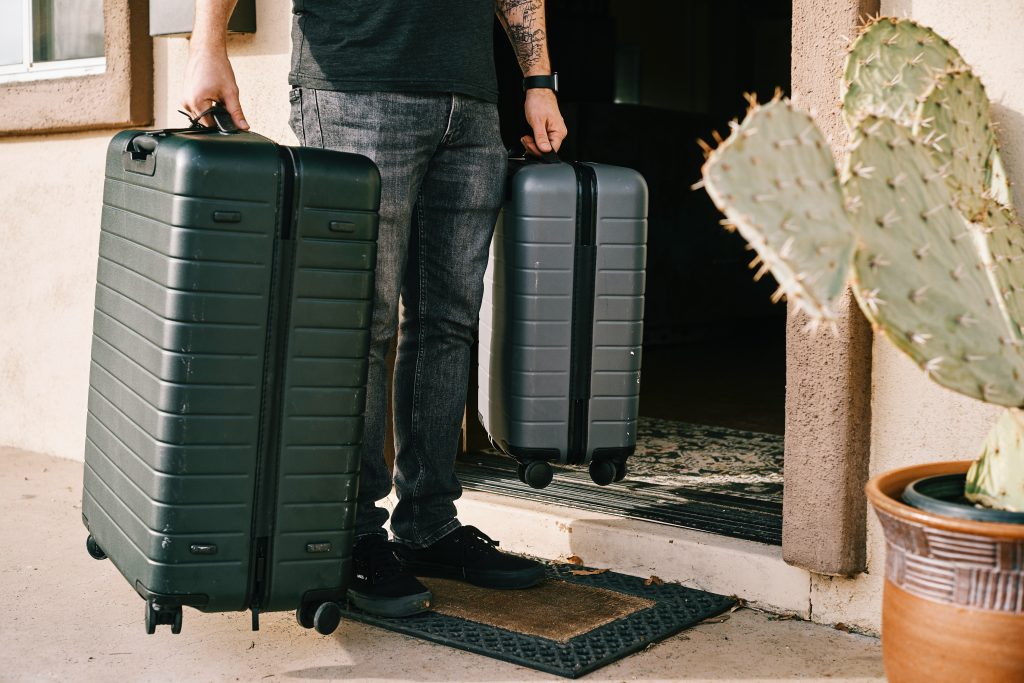man holding two away luggage pieces in the entry of a doorway