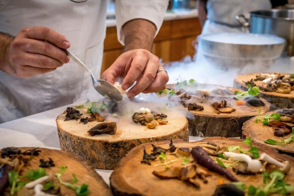 Chef at a Michelin Starred restaurant plating food onto a tree trunk slice plate