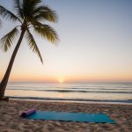 A serene beach at sunset with palm trees, calm ocean waves, and a yoga mat set up on the sand